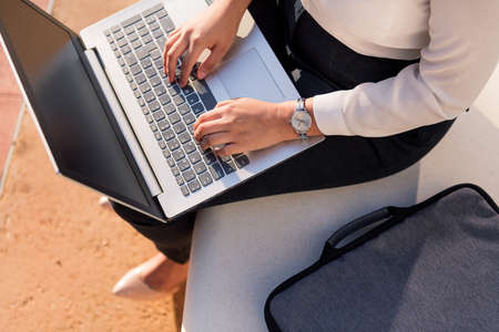 unrecognizable businesswoman typing on her laptop computer sitting in a park in the financial district, concept of digital entrepreneur and urban lifestyleの写真素材