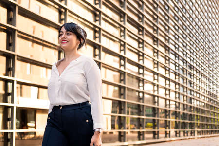 businesswoman walking smiling in front of an office building in the financial district, concept of successful entrepreneur and urban lifestyle, copy space for textの写真素材