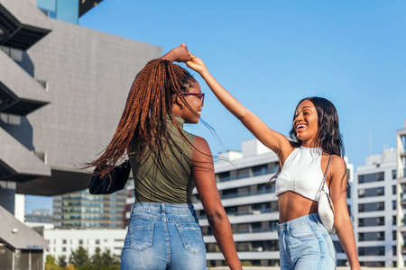 two young african friends dancing in the street holding hands, concept of friendship and urban lifestyleの写真素材