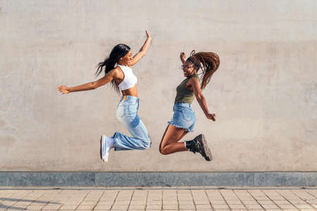 two young african girls jumping happy with a gray concrete wall in the background, concept of friendship and urban lifestyleの写真素材