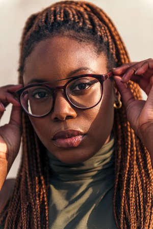 vertical close-up portrait of a young black woman putting on her glasses and looking at the camera, concept of youth and racial diversityの写真素材