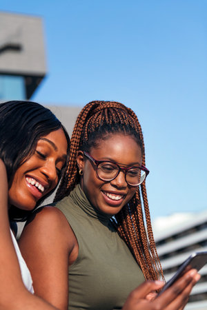 vertical photo of two young black women smiling and having fun looking at the cell phone, concept of youth and communication technology, copy space for textの写真素材
