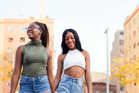 couple of black girls strolling happy in the city holding hands, concept of love and diversity, copy...