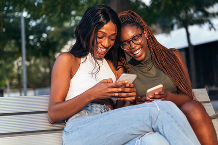 two young black women laugh out loud looking at their social networks on their mobile phones, concept of youth and fun, copy space for textの写真素材