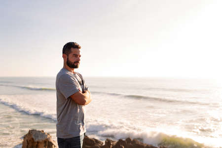 portrait of an attractive man standing watching the sunset from a cliff by the sea, concept of leisure and relax, copy space for textの写真素材