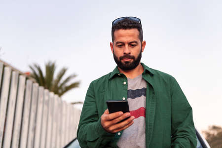 handsome young man with beard consulting mobile phone, leisure and communication technology concept,...