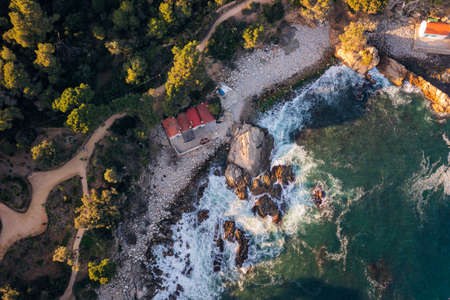 top view of a rocky cove next to a pine forest with some fishermen's huts on the pebble beach, concept of nature and seafaring lifestyleの写真素材