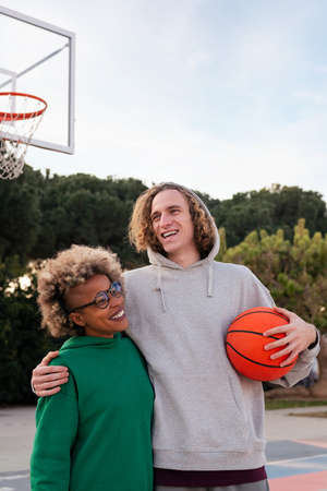 latin woman and caucasian man smiling happy after playing on a city park basketball court, concept...