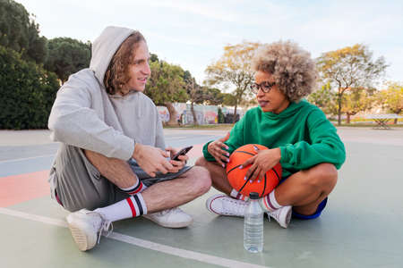 man and woman chat and share a good time sitting on the court after playing basketball at a city park, concept of friendship and urban sport in the streetの写真素材
