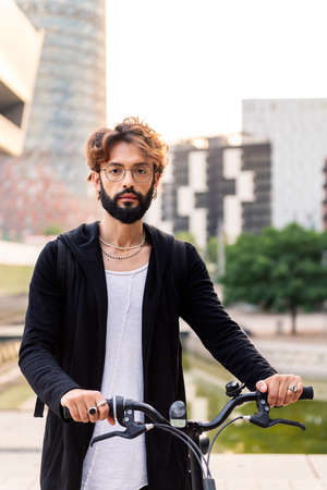 vertical portrait of a young caucasian man holding his bike in the city, concept of urban lifestyle...