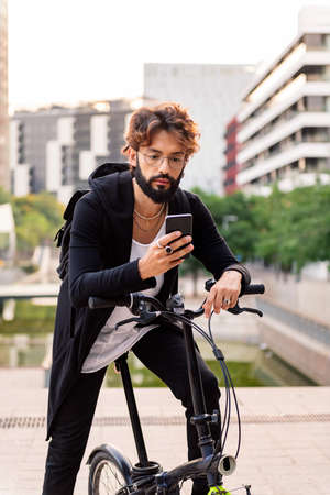 young caucasian man using his mobile phone while sitting on his bike in the city, concept of technology of communication and sustainable mobilityの写真素材
