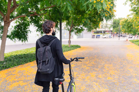 rear view of an unrecognizable young man walking with a folding bike by the city, concept of youth...