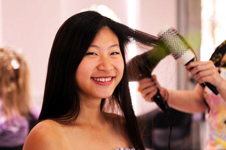 stylist combing womans hair with brush and dryerの写真素材