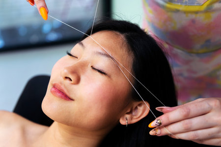 beautician performs eyebrow threading on a womanの写真素材