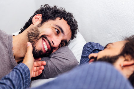 happy male couple relaxing in bed caressing faceの写真素材