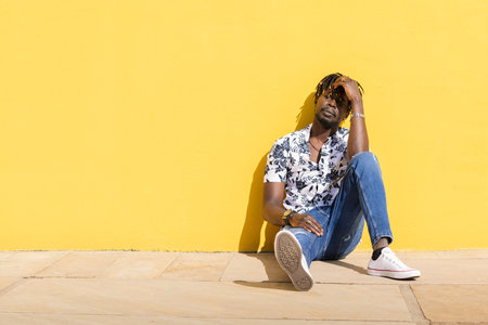 black man sitting on the floor against yellow wallの写真素材