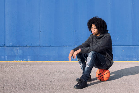 african american teen sitting on basketball ballの写真素材