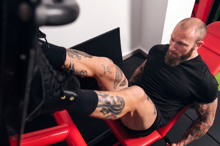 muscular sportsman training on leg press at gym