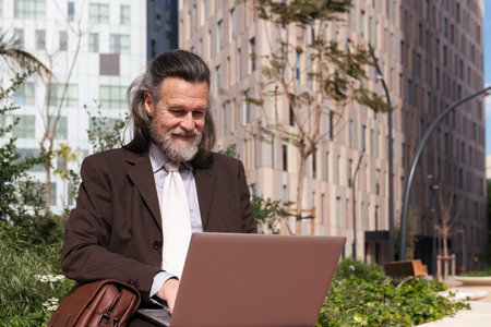 mature male using laptop sitting on urban squareの写真素材