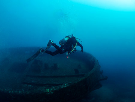 scuba diver diving into the ocean near of a wreckの写真素材