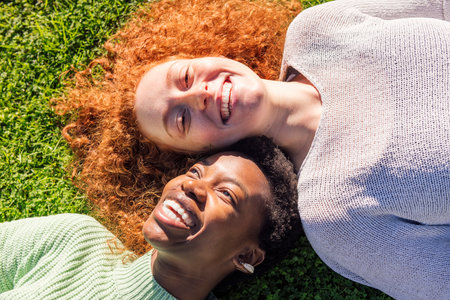 two young women smiling while laying on the grassの写真素材