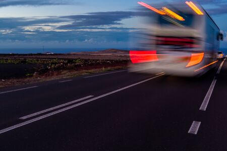 horizontal photography a day about dusk in which a bus moves along the road that guides us to the coast, in the background you can see a small mountain in lanzarote spainの写真素材