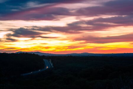 Horizontal landscape photography of the Sierra de Guadarrama, Spain, the photograph is a backlight in which only a car is seen and the vegetation is intuited, the main object is a beautiful sky full of colorsの写真素材