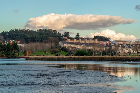horizontal landscape of a day with a blue sky and some cloud, in which we can see the houses near the ria del burgo, the park built on its two banks and the contamination in the form of mud that this beautiful place hasの写真素材