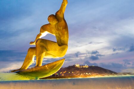 well-known source of coruÃ±a, in front of the riazor beach, in which there is a bronze figure surfing the waves of the source, with the mount of sanpedro in the backgroundの写真素材
