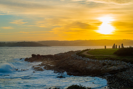 relaxing photograph of a sunset overlooking the choppy sea in front of the stillness of the menhirs and the coastlineの写真素材