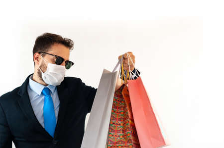 Stylish man in a suit with mask and sunglasses holding and looking at shopping bags. Black friday concept.の写真素材