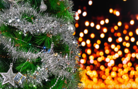 Green Christmas tree with silver glitter decoration on a background of yellow unfocused lights with copy space. Selective focus.の写真素材