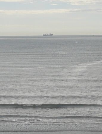 Beach coast with grayish sky, boats, calm sea, rainy sunrise