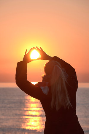 Blonde girl from the back catching the sun, sunrise, no clouds, black coat, hair upの写真素材