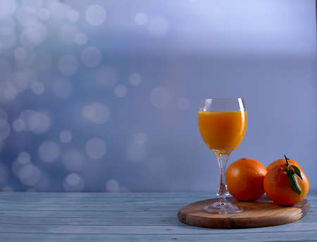Glass of orange juice with various oranges on wooden table on bright background and wooden floor, free space, front viewの写真素材