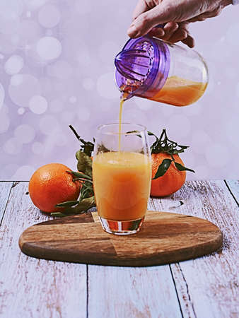Hand pouring orange juice into glass with glass squeezer, wooden table, wooden floor bright backgroundの写真素材