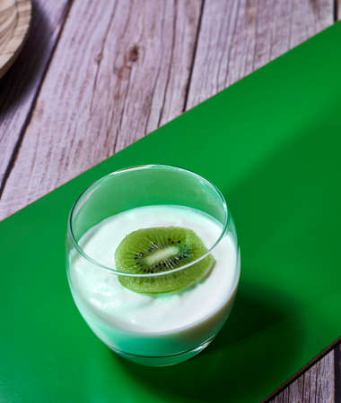 Glass of yoghurt with a sliced kiwi. Diagonal green wooden board, wooden planksの写真素材