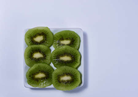 Halved kiwis on a rectangular plate, white and bright background, symmetry, empty space, zenithal viewの写真素材