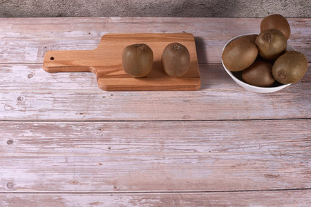 Various kiwis in white bowl and wooden board. Wooden boards, empty space, frontal view, warm tones