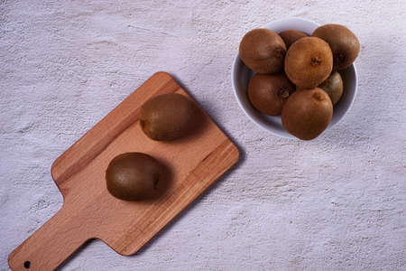 Kiwis on wooden chopping board. Stone background, bowl with several kiwis, empty space, zenithal view.の写真素材