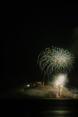 Experience the dazzling display of fireworks illuminating the skyline of Peniscola, captured with precision through a telephoto lens, as bursts of color dance above the city, painting the night sky with a mesmerizing symphony of light and magicの写真素材