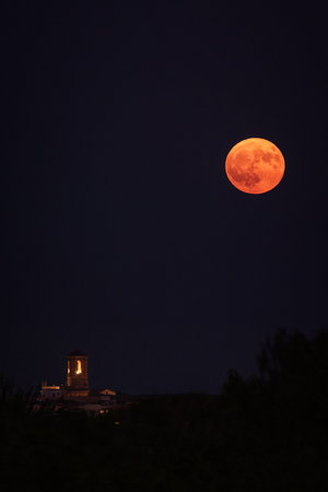 Illuminated church tower, reddish full moon.の写真素材
