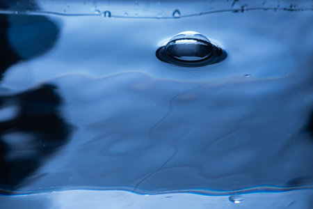 222.Spherical bubble protrudes above smooth blue water surface. Subtle ripples and reflections...