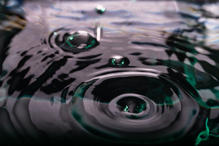 375.Close-up of dark water surface with ripples and bubbles. Droplet impacts create concentric circles. Lighting adds reflections and texture. Image shows fluid motion and surface tension.の写真素材