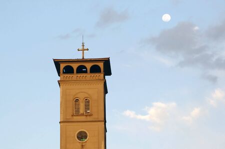 Church tower with a cross in top in a cloudy sky and Moon background.の写真素材