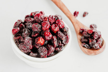 Dried Cranberries in a White Bowl with Wooden Spoon on White Background Low Angle Photoの写真素材