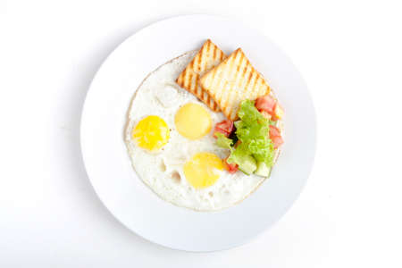 fried eggs with fried toast and salad of fresh cucumbers and tomatoes with herbsの写真素材