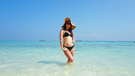 Girl in hat and swimsuit on the beach. Glasses on. European woman on the beach with white sand. The water is turquoise with a blue tint. Photo shoot model. Paradiseの写真素材
