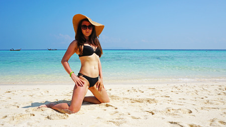 Girl in hat and swimsuit on the beach. Glasses on. European woman on the beach with white sand. The water is turquoise with a blue tint. Photo shoot model. Paradiseの写真素材