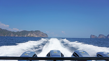 View of the back of the boat. Waves from the engines of a high-speed boat. It offers a landscape of sea, green hills and blue sky. White clouds hung over the Islands. Travel by sea.の写真素材
